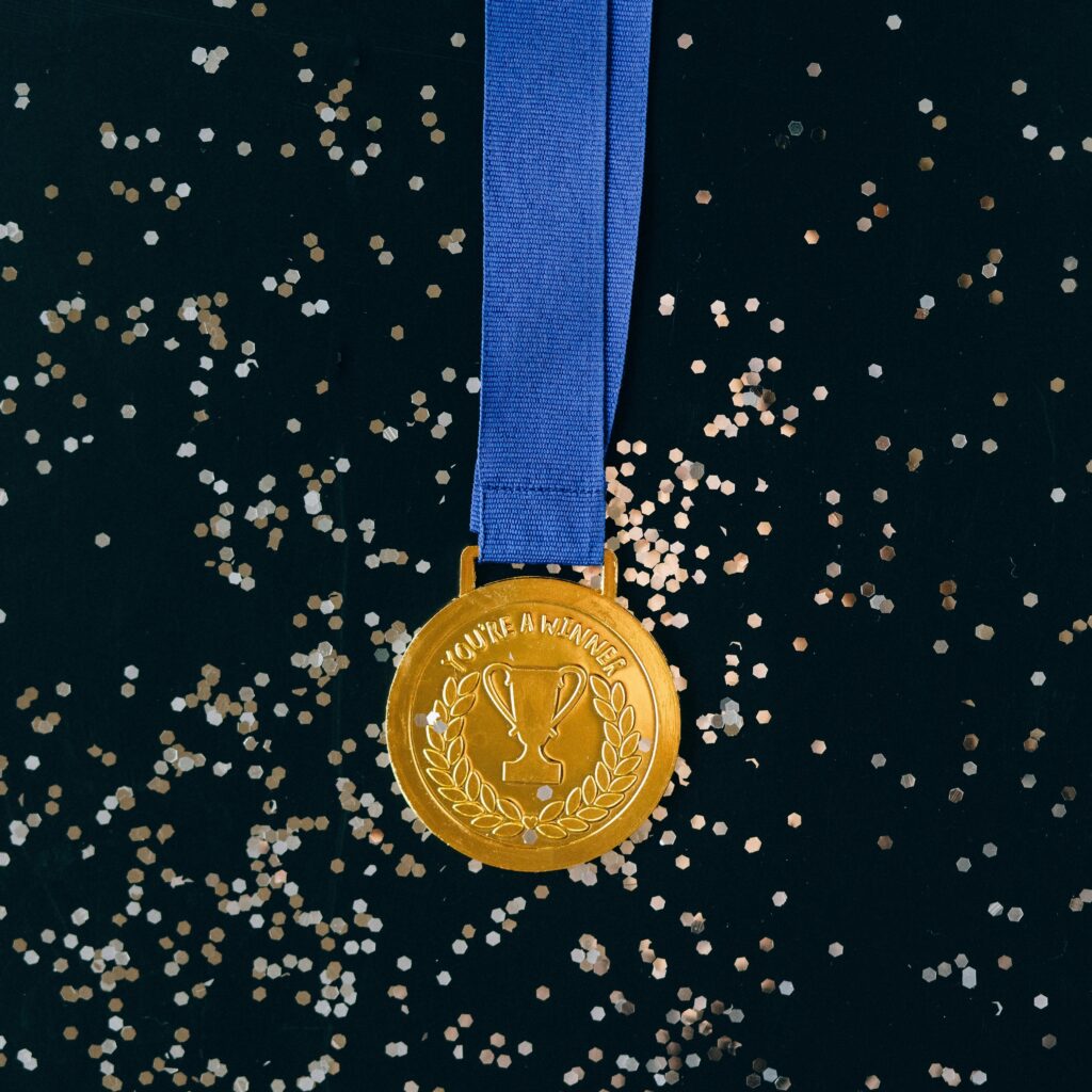 pexels-photo-6120397-6120397 Close-up of a shimmering gold medal with blue ribbon on a black surface, symbolizing victory and achievement.